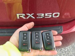 A hand holding three keys in front of a red car.
