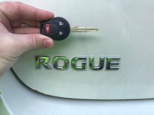 A person holding a car key in front of the word rogue.